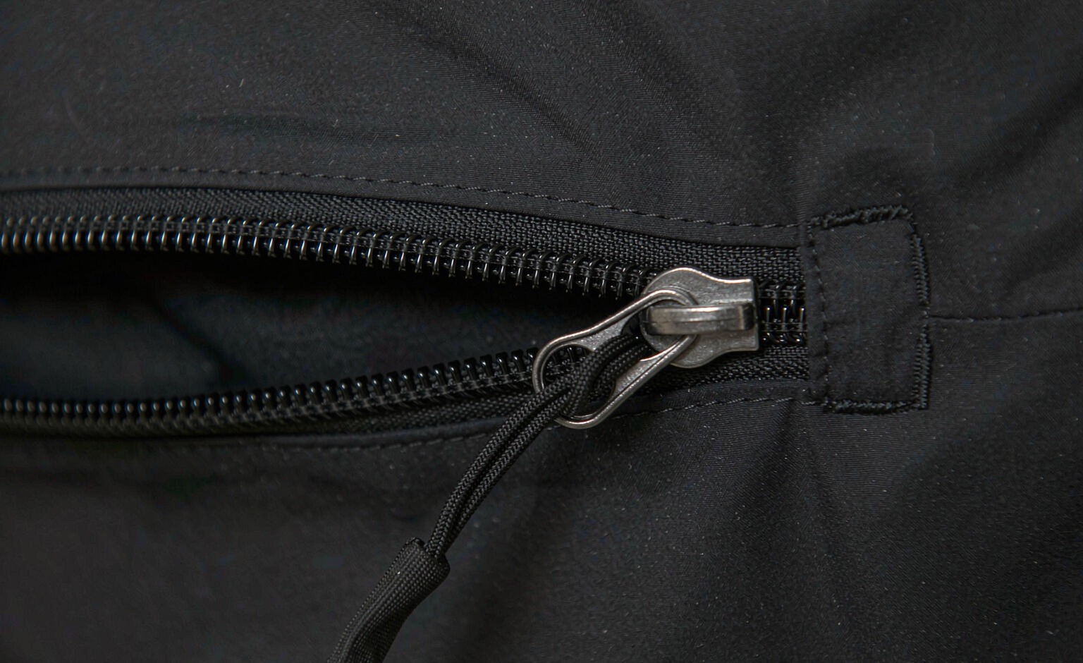Macro view of a coated coil zipper with a cord puller on a technical fabric panel