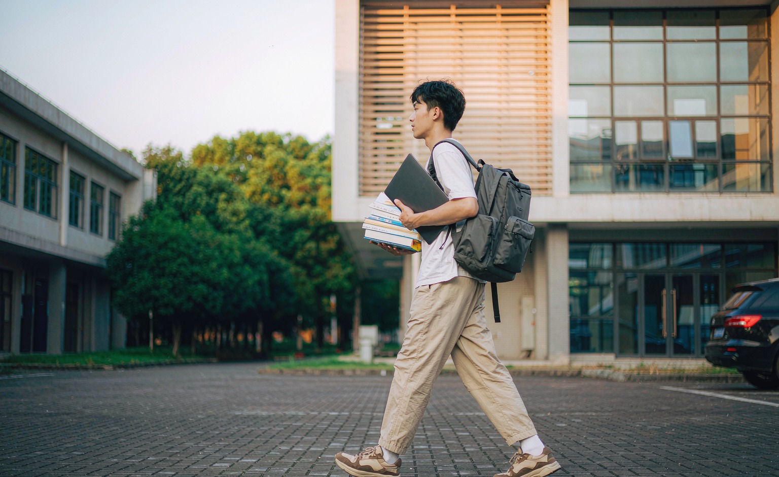 Student walking across a campus quad wearing a modular backpack with a detachable side pouch
